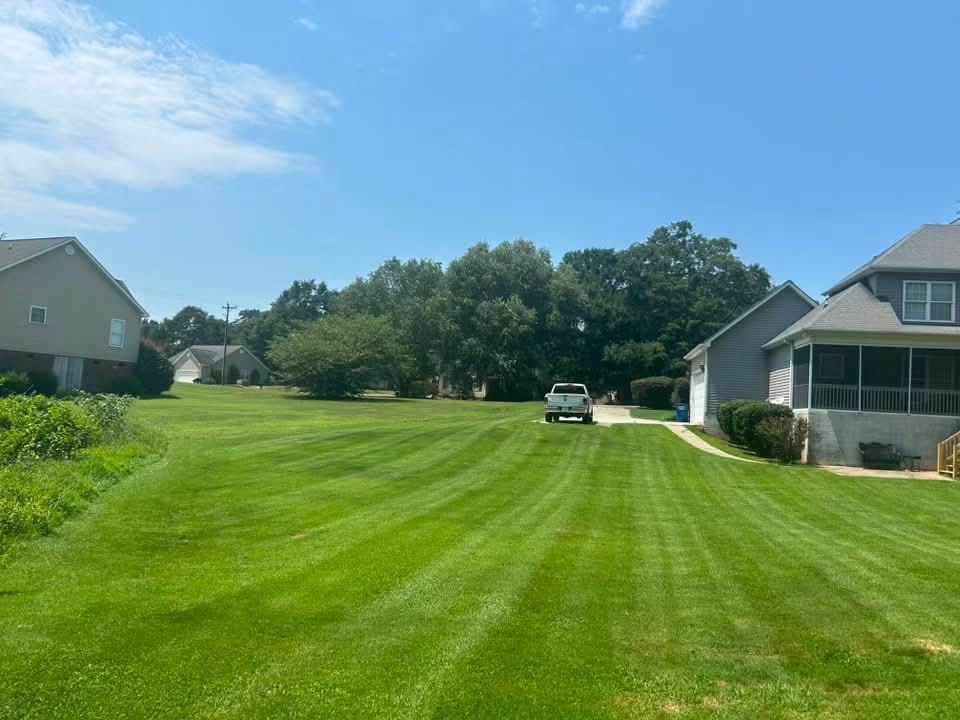 A freshly mowed residential lawn with crisp striping between two houses, with a truck parked in the driveway