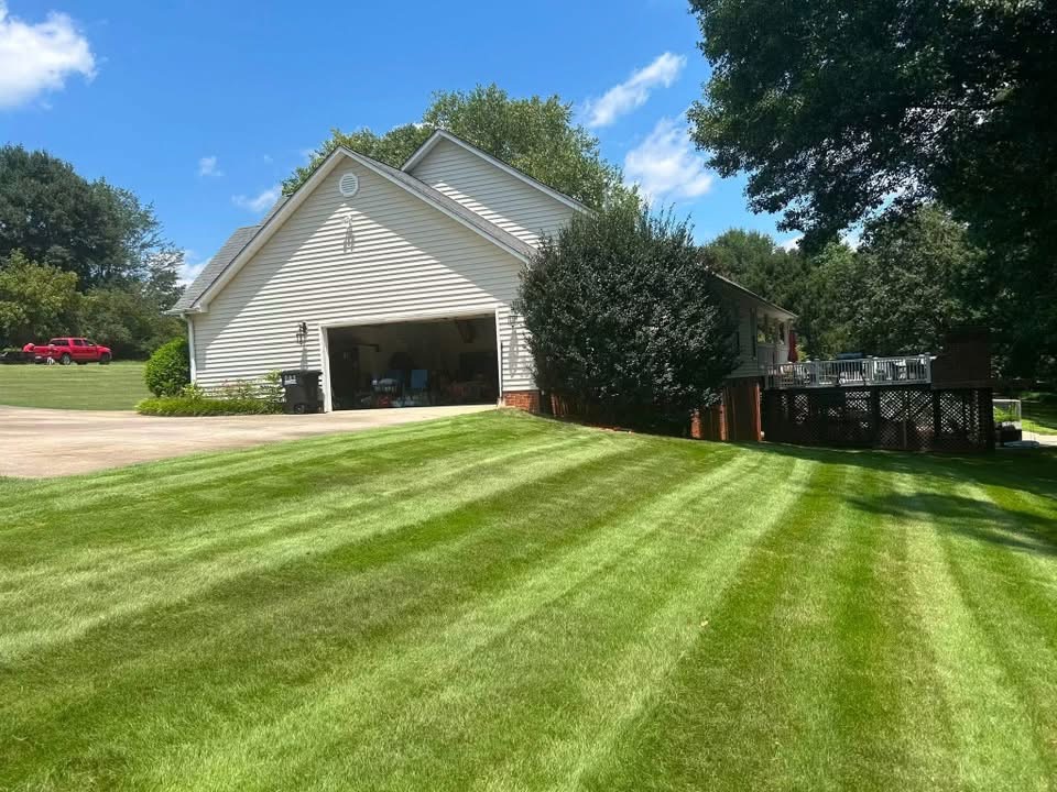 A freshly mowed residential lawn with crisp striping beside a garage with an open bay door and a paved driveway